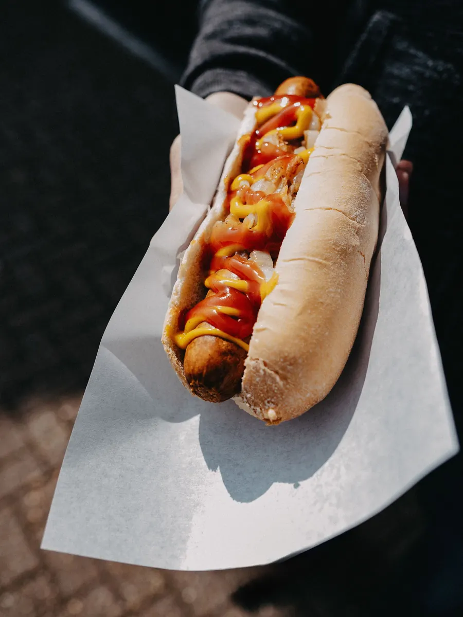 Hand holding a hot dog with ketchup and mustard